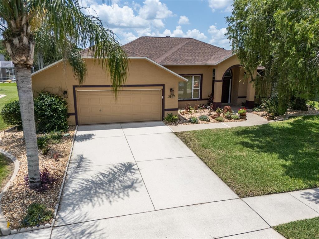A single-story house with a tan stucco exterior, a two-car garage, and a landscaped front yard — 1887 CREEKWATER BOULEVARD, PORT ORANGE, FL