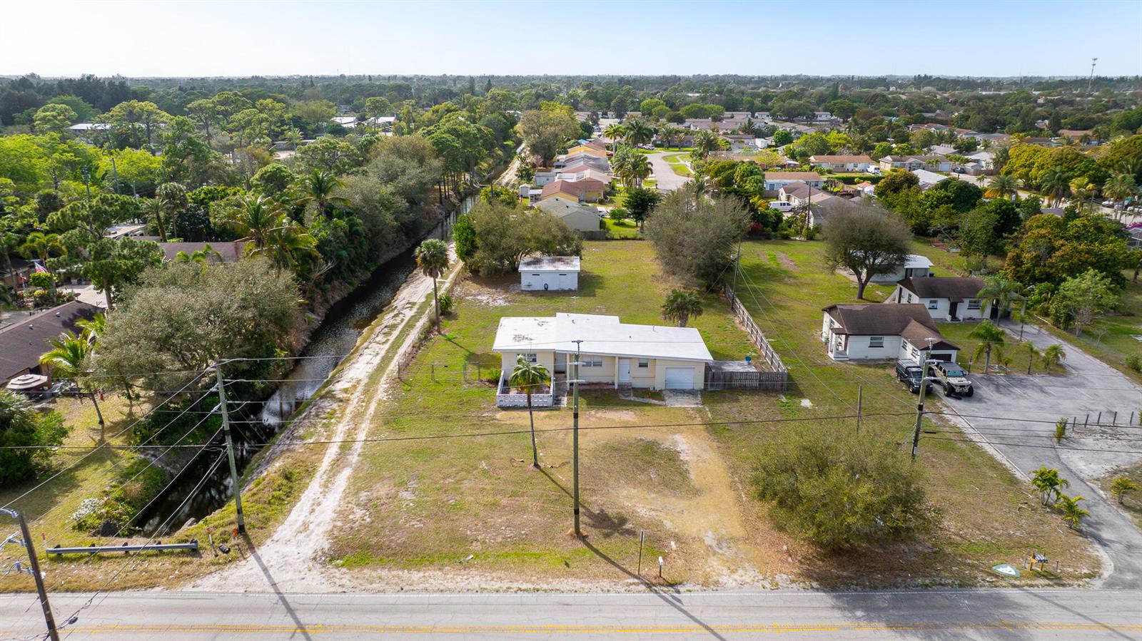 An aerial view shows a single-story house with a white roof beside a drainage canal — 4475 Kirk Road, Lake Worth FL 33461, LAKE WORTH, FL