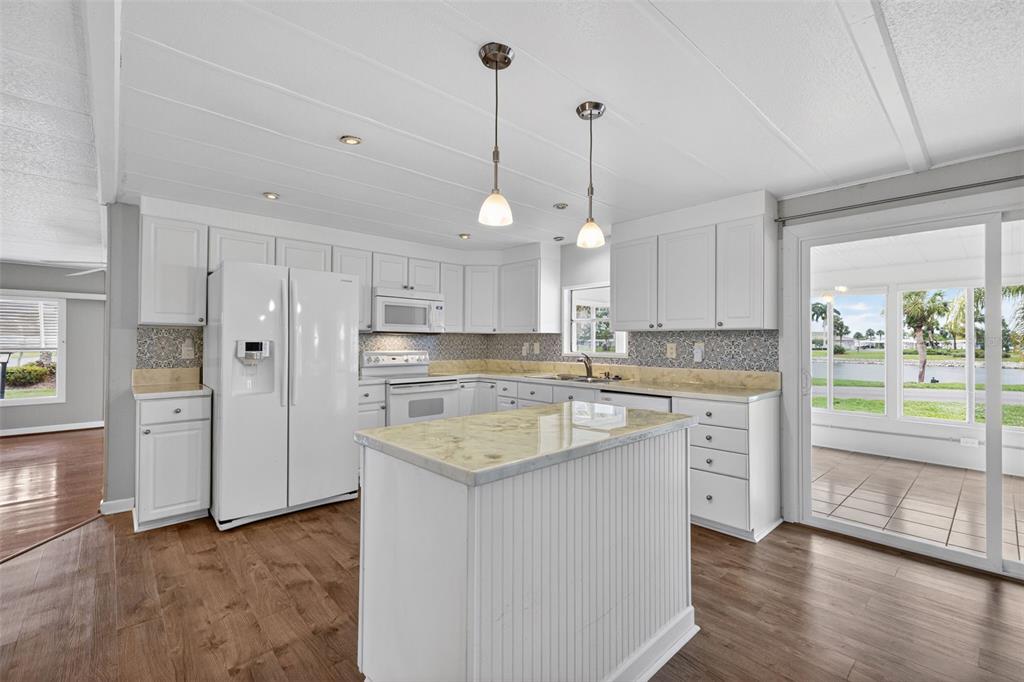 A white kitchen with an island, stone countertops, and a sliding glass door to a patio — 401 LOMA LINDA, NORTH PORT, FL