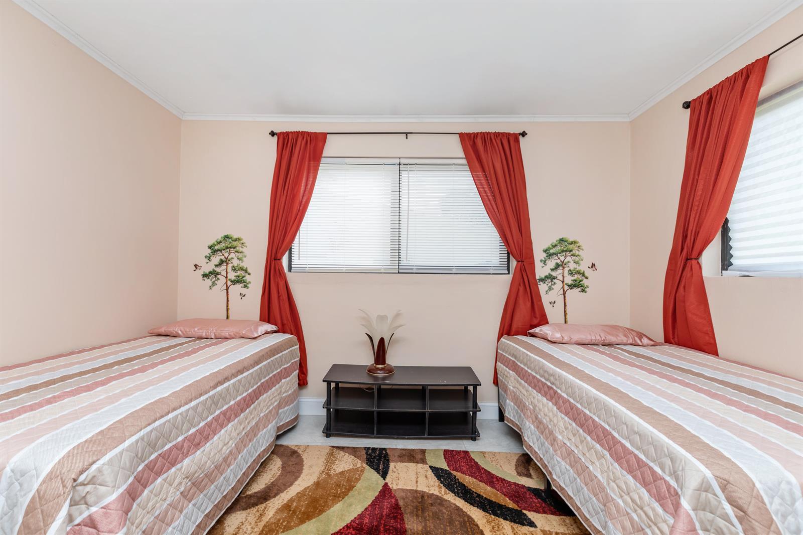 A bedroom features two twin beds, red curtains, a central media console, and patterned carpeting — 475 NE 113th Street, Miami FL 33161, MIAMI, FL