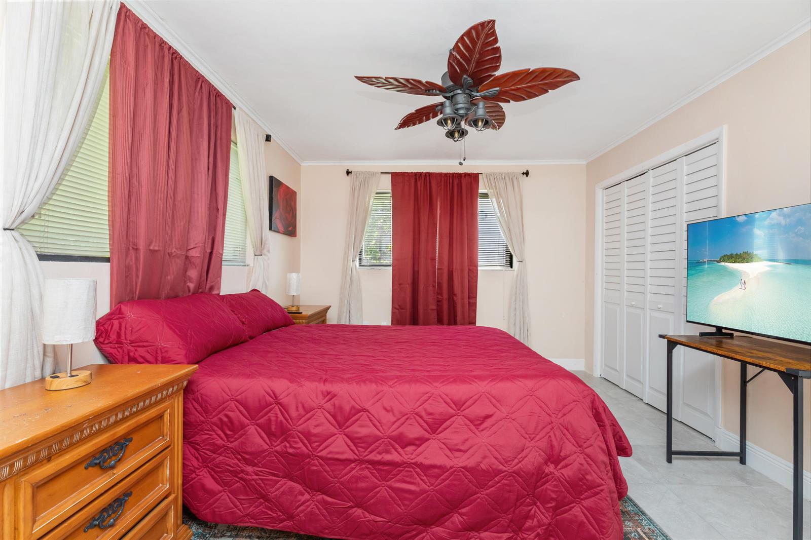 A bedroom features a red bedspread, wooden furniture, a ceiling fan, and a television — 475 NE 113th Street, Miami FL 33161, MIAMI, FL