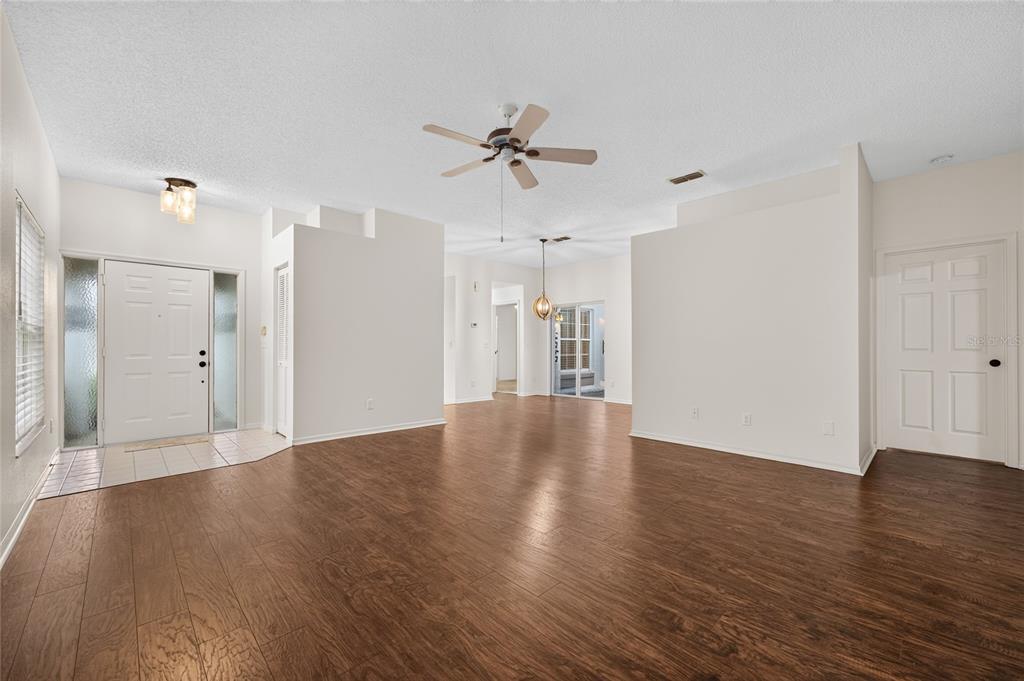 A spacious living room with wood-look flooring, white walls, a ceiling fan, and an entryway — 11206 PURPLE PLUM COURT, ORLANDO, FL