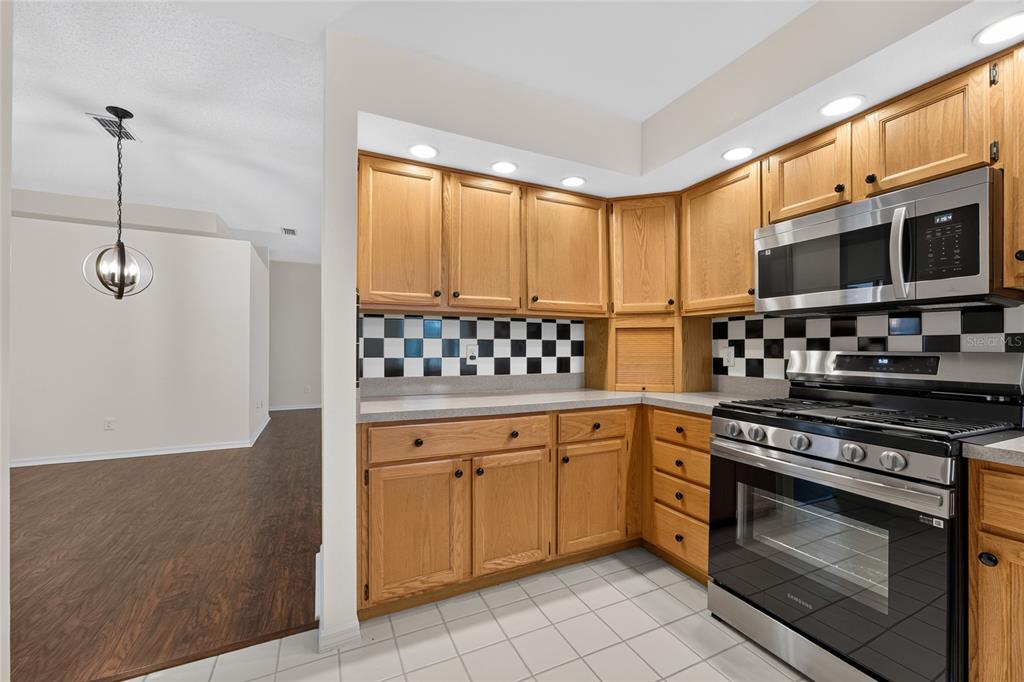 A kitchen with oak cabinets, a black and white checkered backsplash, and stainless steel appliances — 11206 PURPLE PLUM COURT, ORLANDO, FL