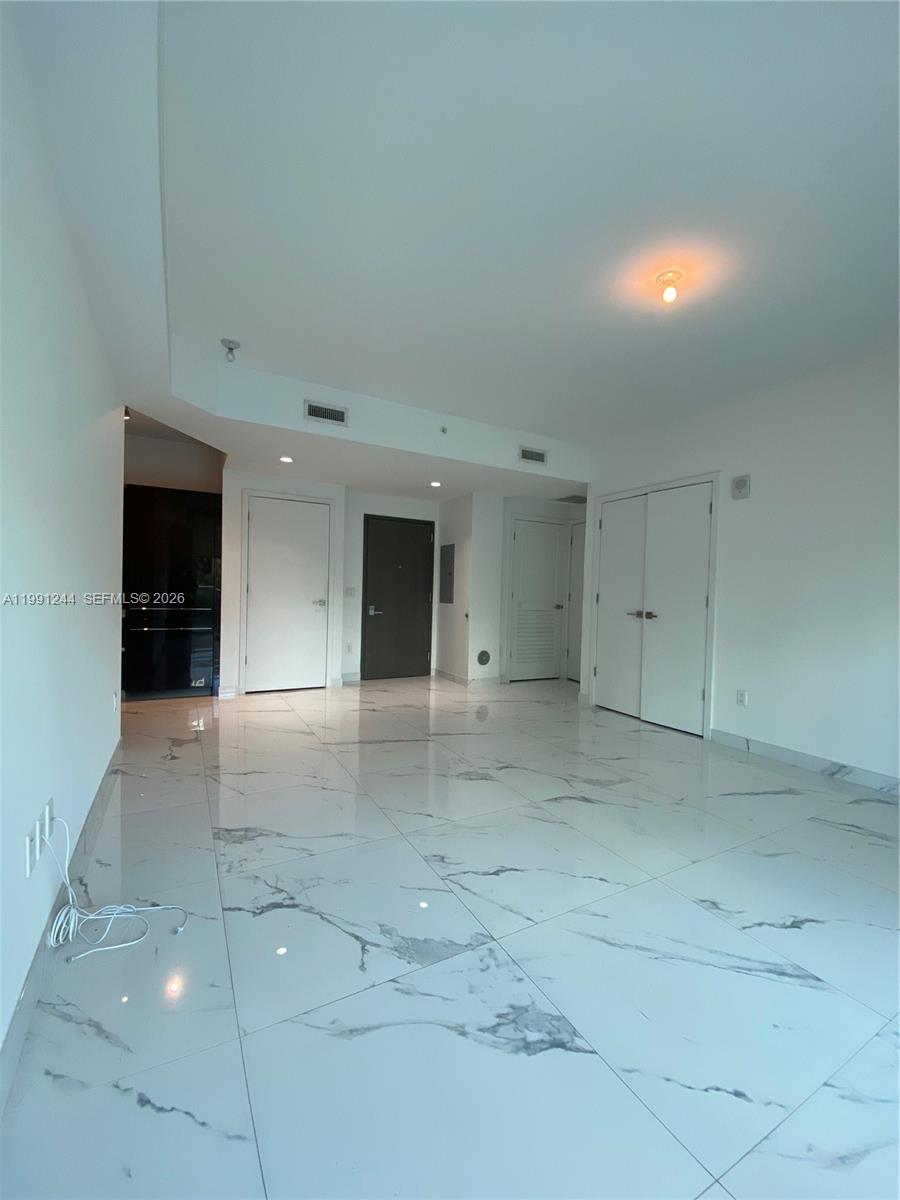 An empty room features white marble-patterned tile flooring, white walls, and several closed doors — 1080 Brickell Ave # 205, Miami FL 33131, MIAMI, FL