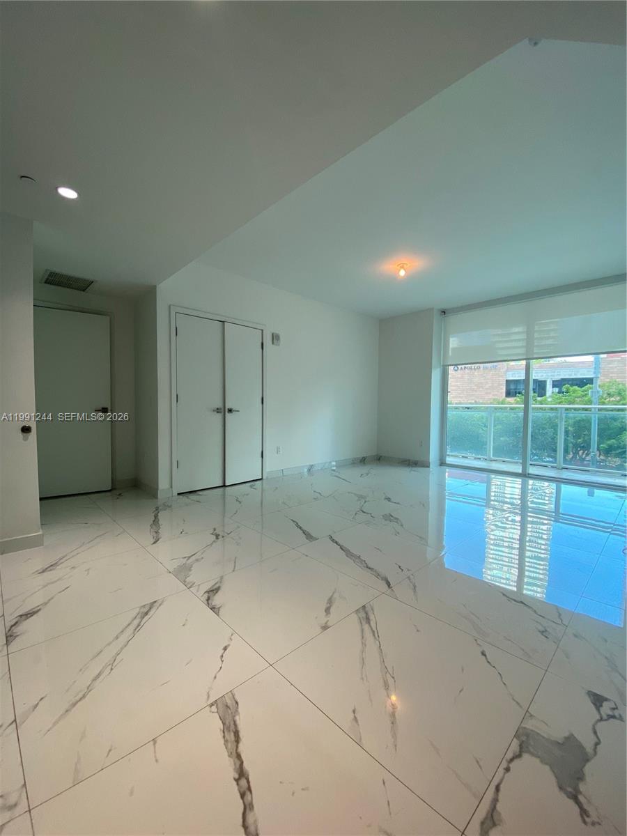 An empty room features white marble-patterned tile flooring, white walls, and a glass balcony door — 1080 Brickell Ave # 205, Miami FL 33131, MIAMI, FL