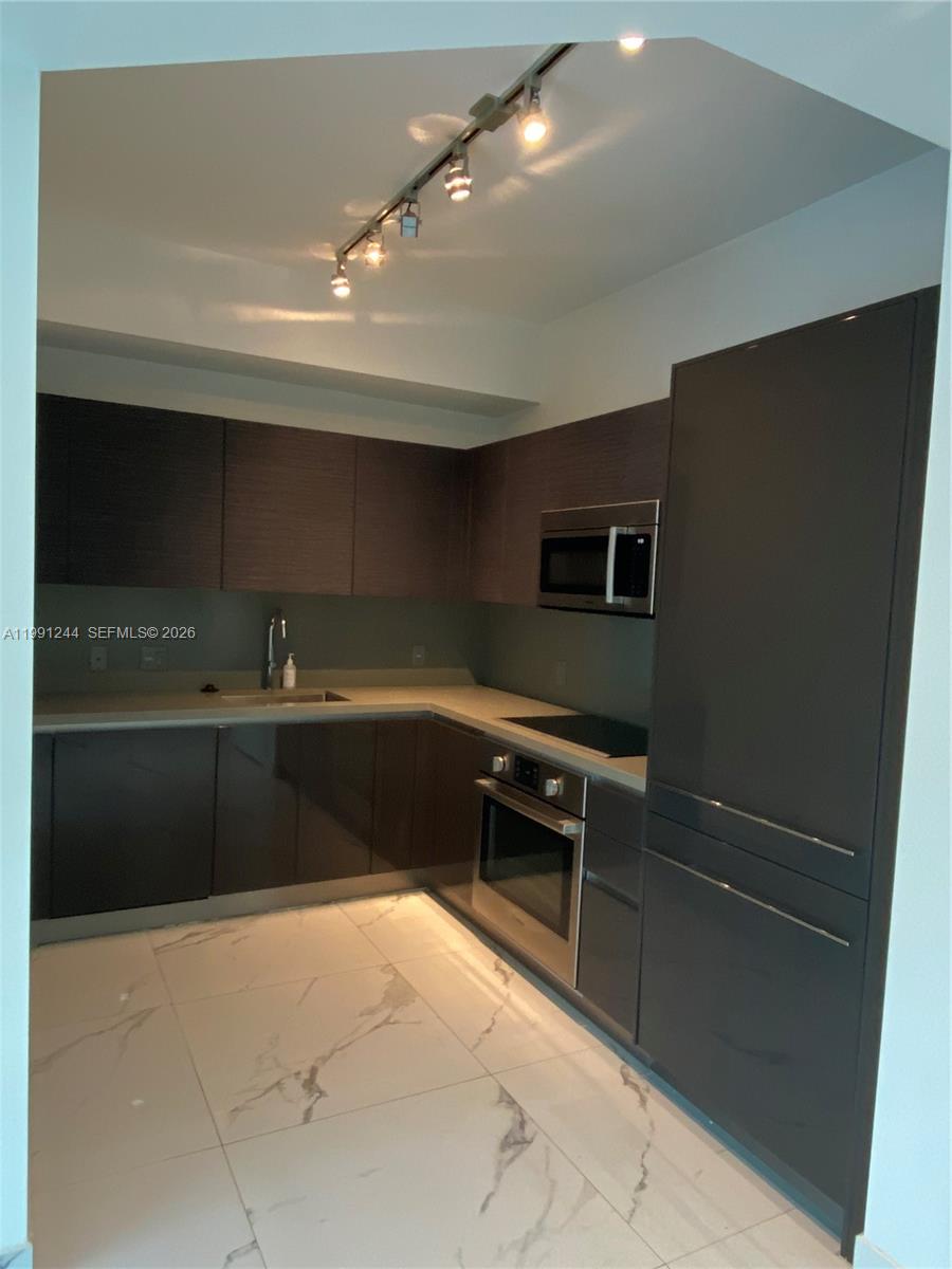 A modern kitchen features dark cabinetry, stainless steel appliances, and white marble-patterned tile flooring — 1080 Brickell Ave # 205, Miami FL 33131, MIAMI, FL