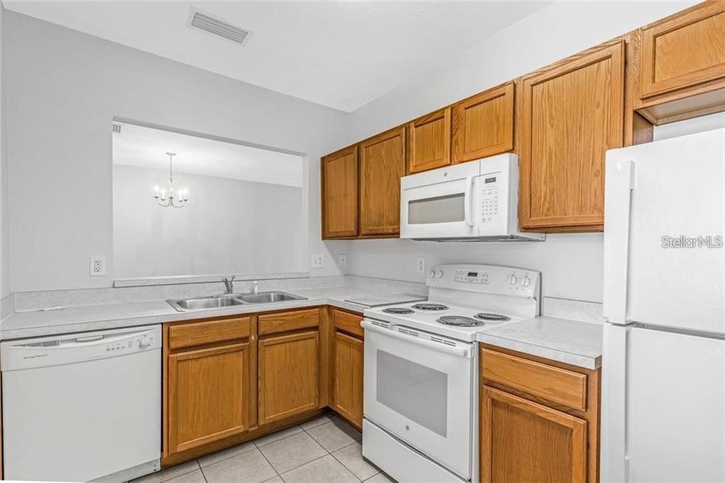 A kitchen with oak cabinets, white appliances, and a pass-through window to the dining area — 9519 NEWDALE WAY UNIT 201, RIVERVIEW, FL