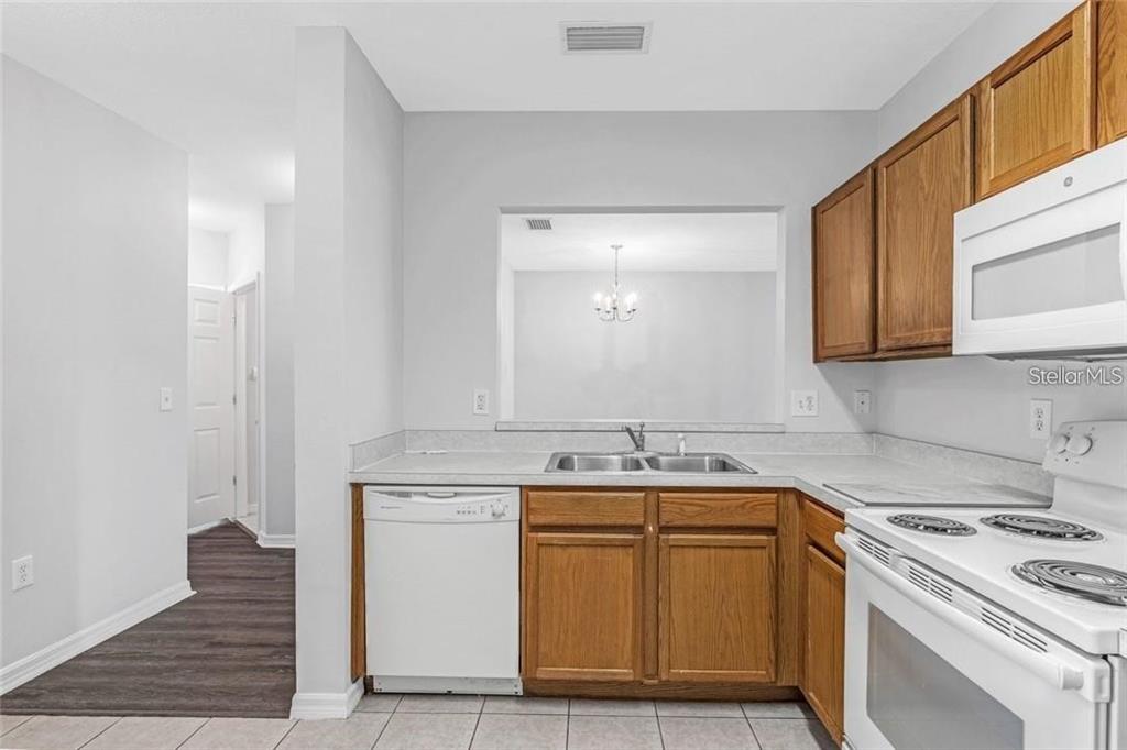 A kitchen features wood cabinets, white appliances, a double sink, and a pass-through window — 9519 NEWDALE WAY UNIT 201, RIVERVIEW, FL