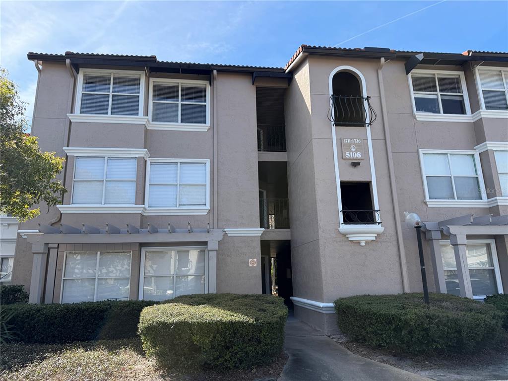 A three-story apartment building with beige stucco walls, white trim, and a central stairwell — 5108 CONROY ROAD UNIT 1713, ORLANDO, FL