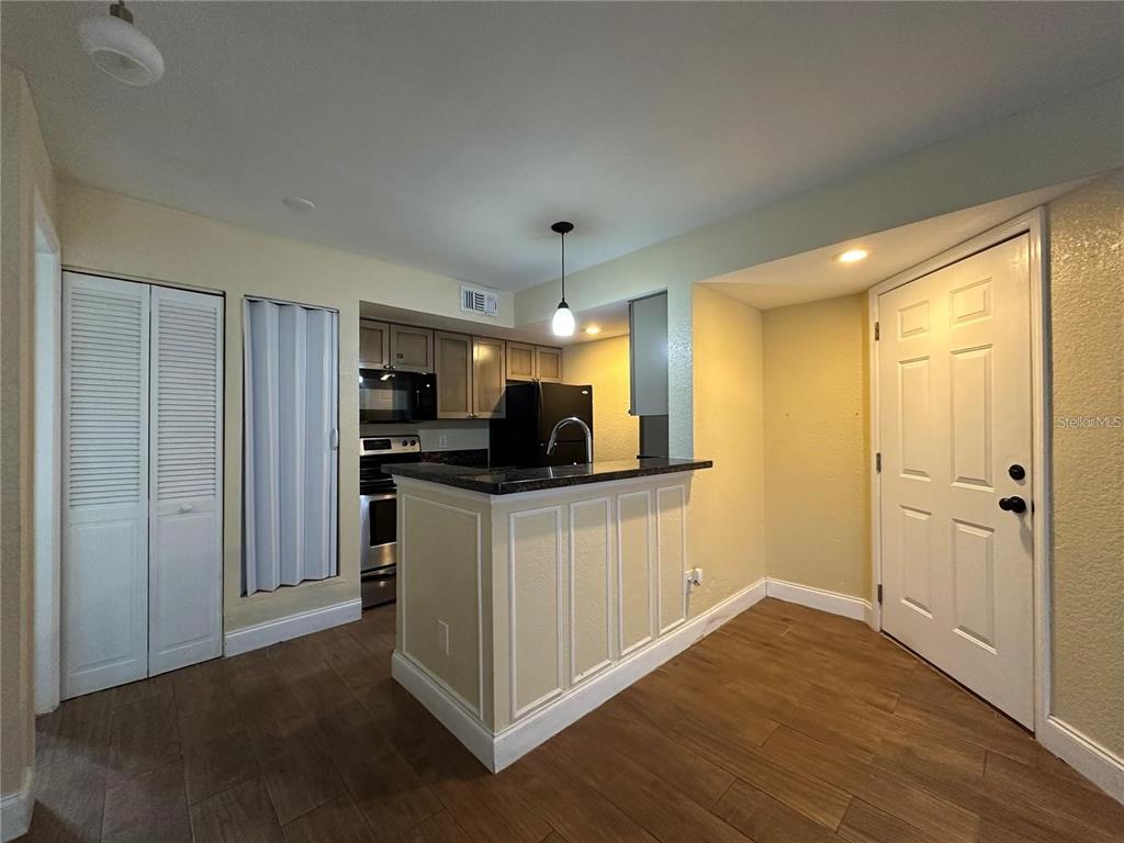 A kitchen features a breakfast bar, dark countertops, wood-look flooring, and a white entry door — 5108 CONROY ROAD UNIT 1713, ORLANDO, FL