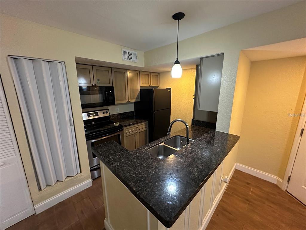 A kitchen features dark granite countertops, light wood cabinets, black appliances, and a pendant light — 5108 CONROY ROAD UNIT 1713, ORLANDO, FL