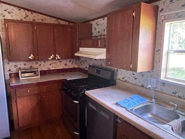 A kitchen features wood cabinets, floral wallpaper, a gas stove, and a stainless steel sink — 7196 NW 205TH STREET, ALACHUA, FL