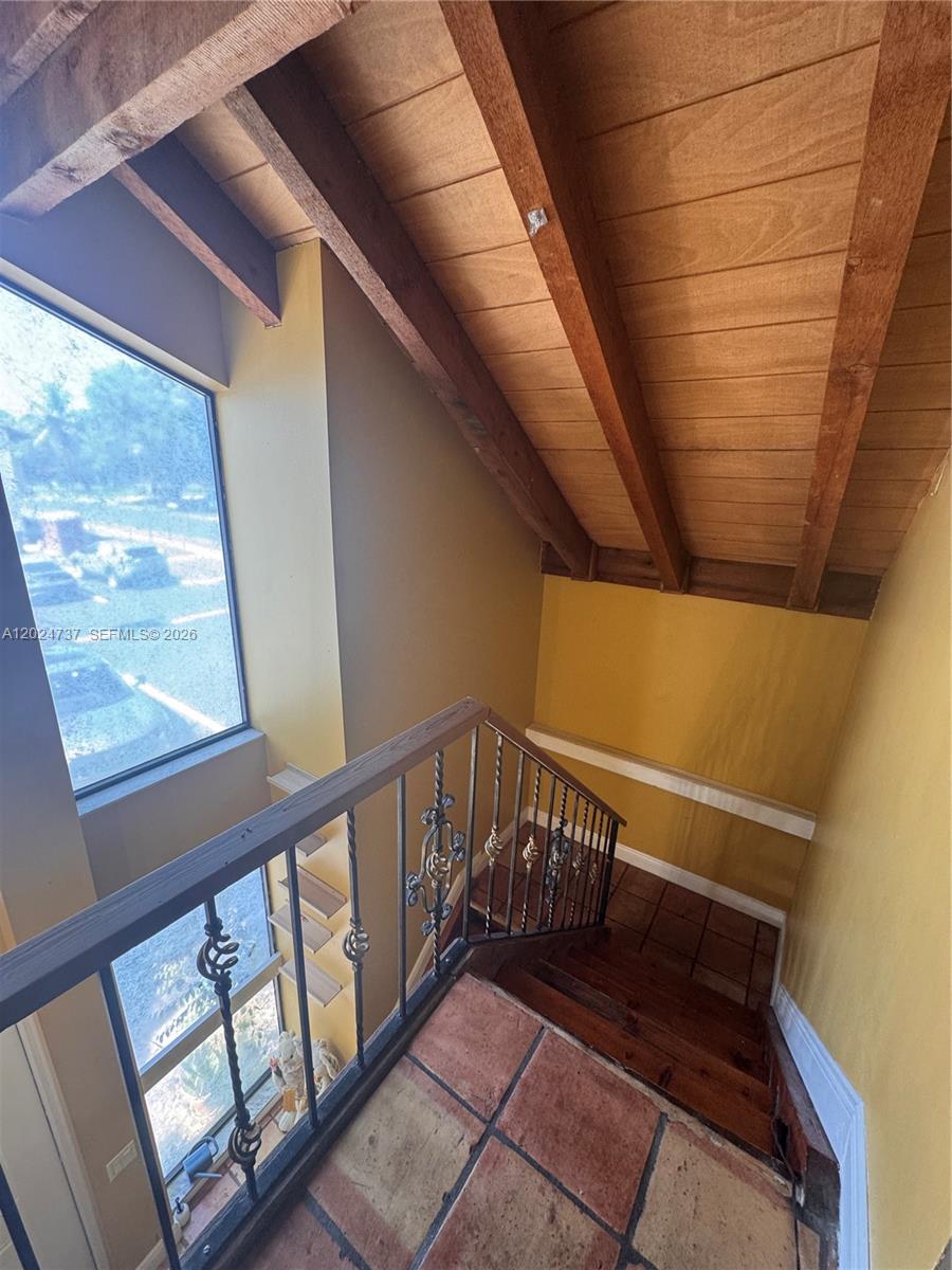 A staircase with wrought iron railings leads down to a tiled landing under wood-beamed ceilings — 6547 SW 116th Pl # C, Miami FL 33173, MIAMI, FL