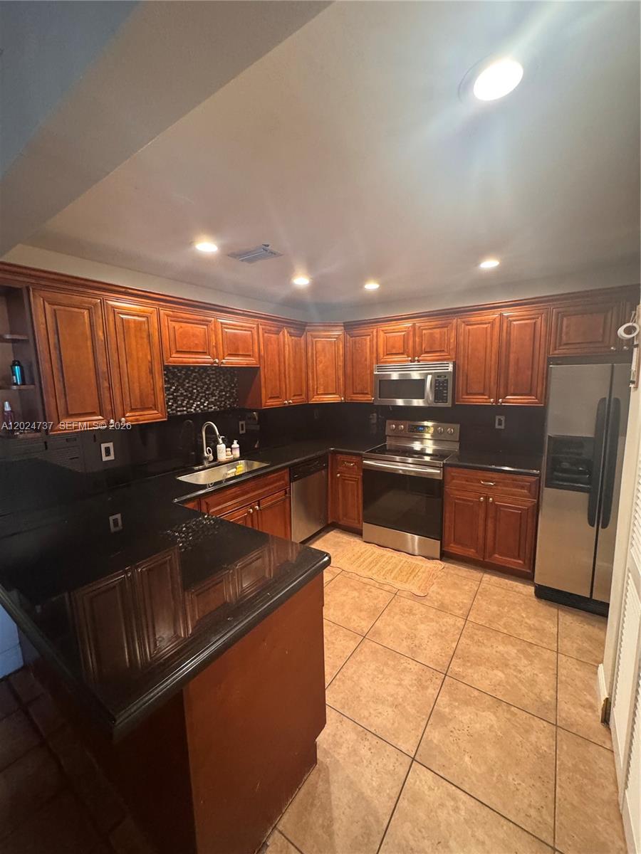 A kitchen features dark wood cabinets, black countertops, stainless steel appliances, and tiled flooring — 6547 SW 116th Pl # C, Miami FL 33173, MIAMI, FL