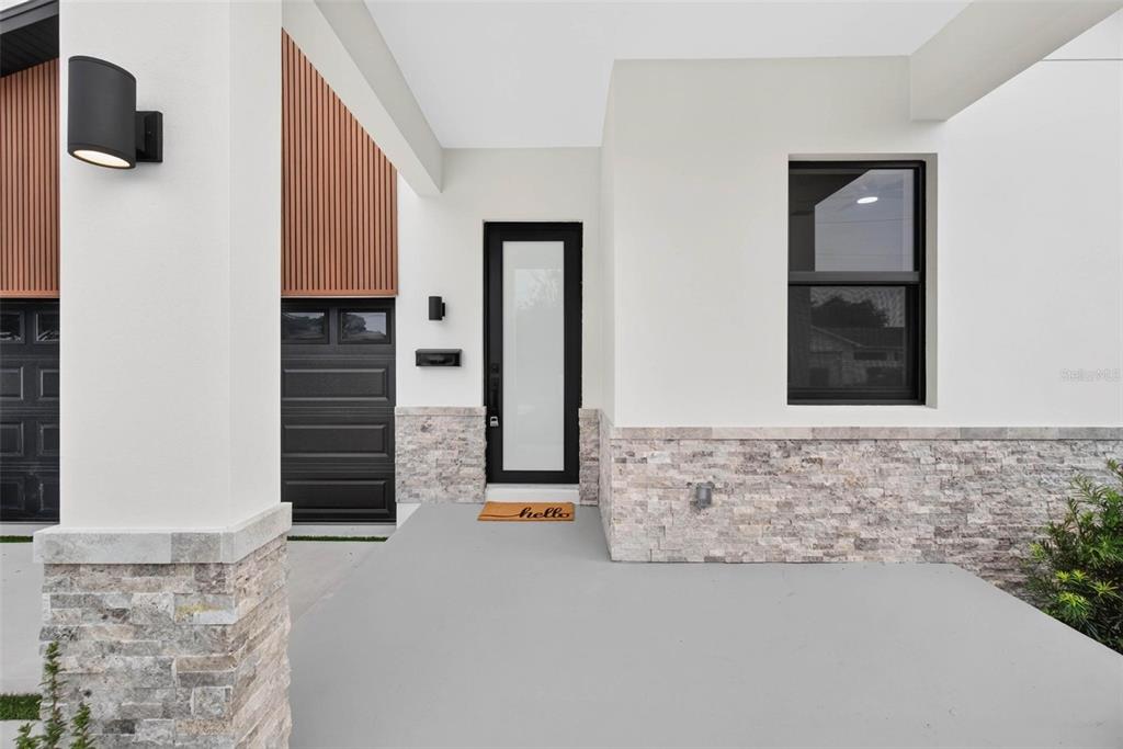 A modern home exterior features a covered porch, stone veneer base, and a glass front door — 2227 32ND AVENUE N, ST PETERSBURG, FL