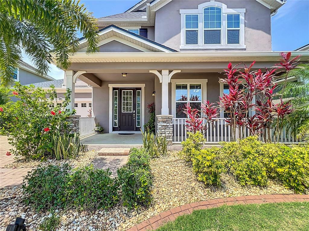 The exterior of a two-story house features a covered front porch, stone pillars, and landscaping — 8054 BUSHMASTER AVENUE, ORLANDO, FL