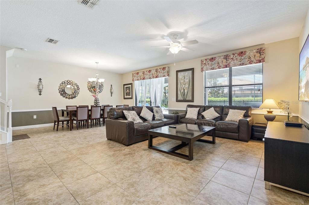 A spacious open-concept living and dining area features tile flooring, dark leather furniture, and windows — 1420 MOON VALLEY, DAVENPORT, FL