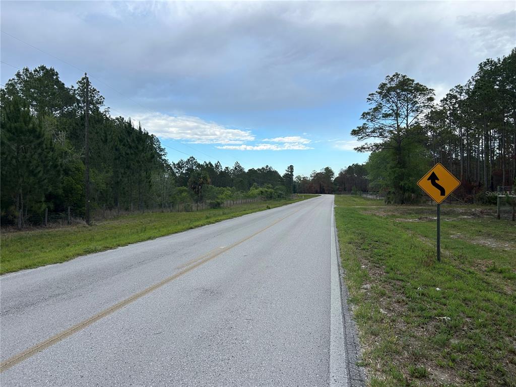 A paved road stretches into the distance past a roadside curve warning sign and trees — 0000 SE 60TH AVENUE, MORRISTON, FL