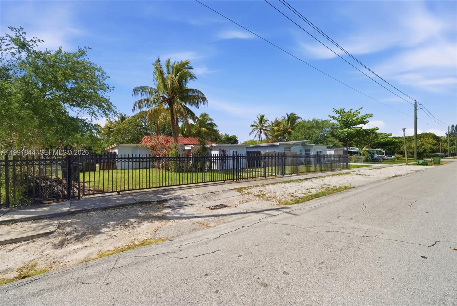 A black metal fence encloses a grassy yard with palm trees in front of houses — 60 NW 128th St, North Miami FL 33168, NORTH MIAMI, FL
