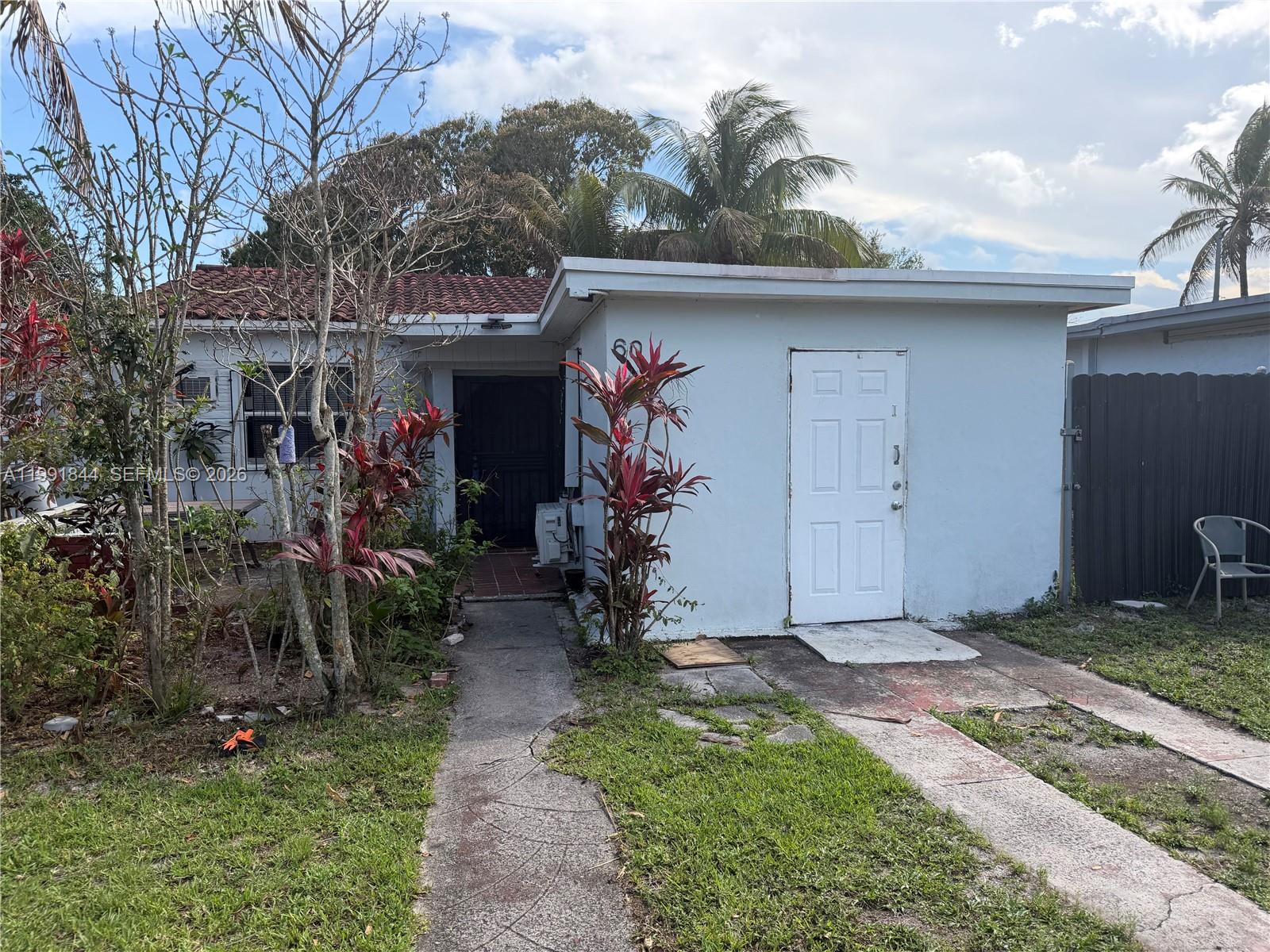 A single-story white house features a front walkway, a white door, and red-leafed plants — 60 NW 128th St, North Miami FL 33168, NORTH MIAMI, FL