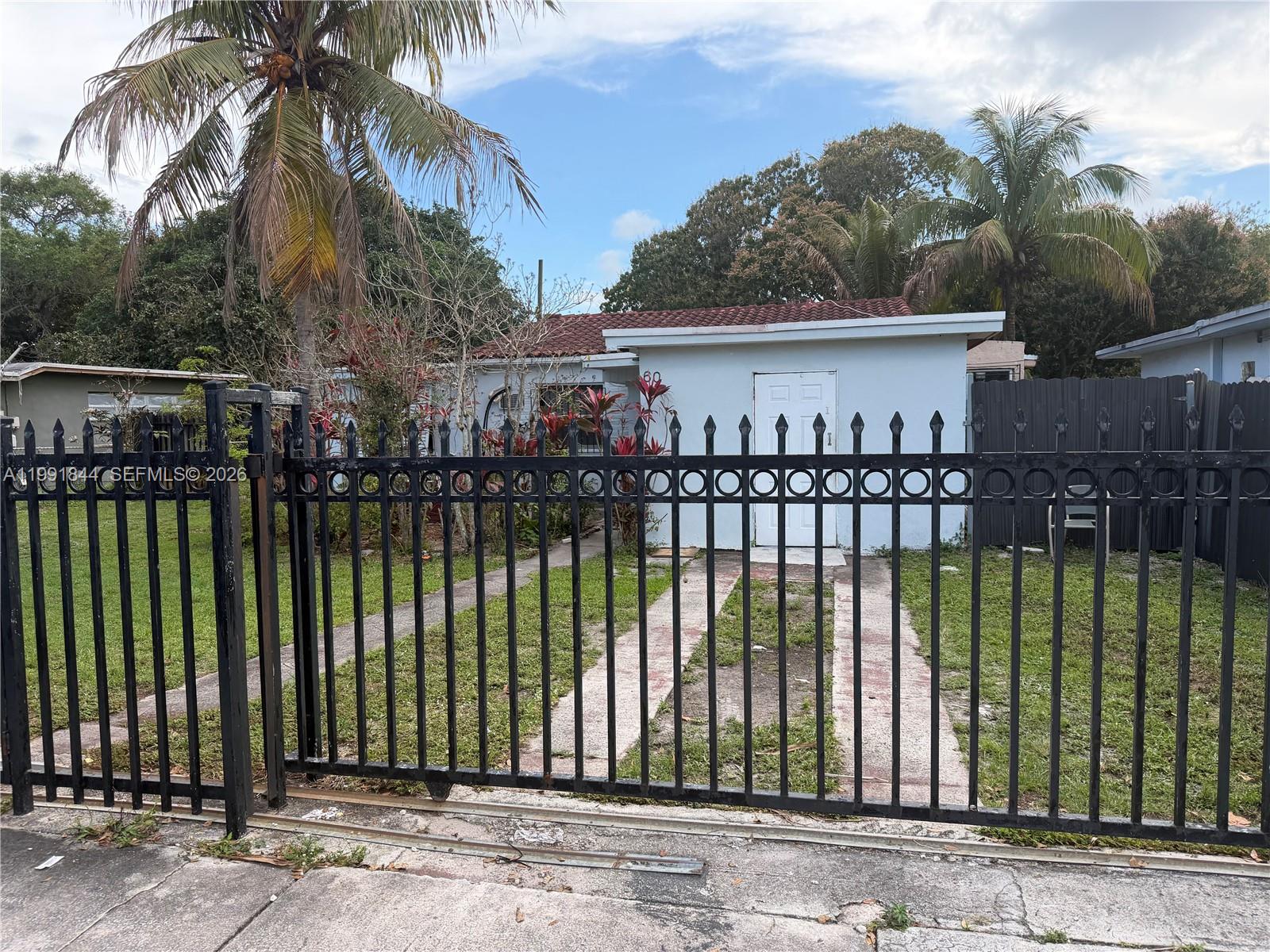 A single-story house with a white exterior and a red tile roof behind a fence — 60 NW 128th St, North Miami FL 33168, NORTH MIAMI, FL