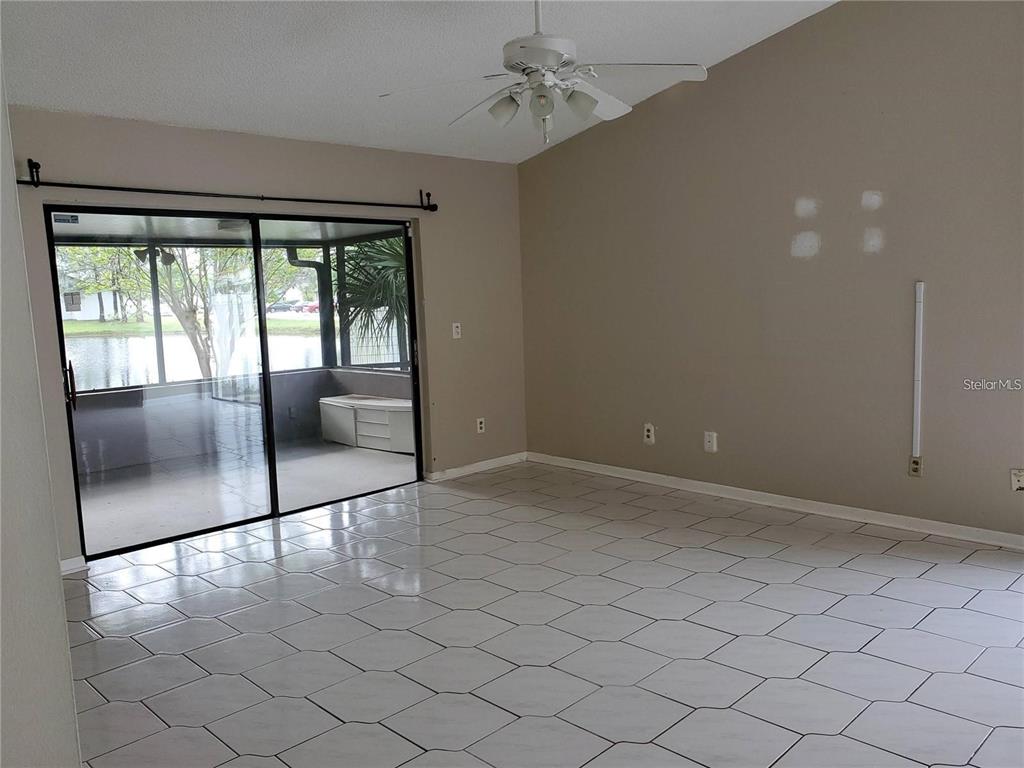 A living room with white tile flooring, a ceiling fan, and sliding glass doors — 11301 DAREWOOD PLACE, TAMPA, FL