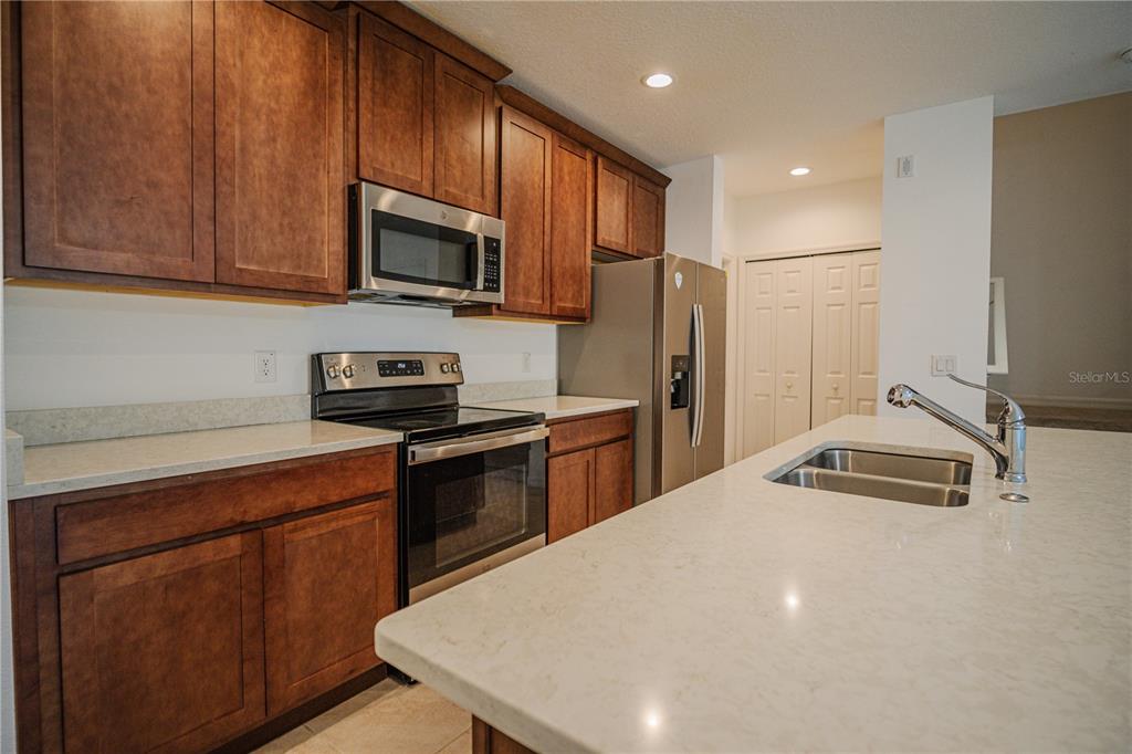 A kitchen features wood cabinets, stainless steel appliances, and a white quartz-topped island — 1284 WISPY CYPRESS DRIVE, KISSIMMEE, FL
