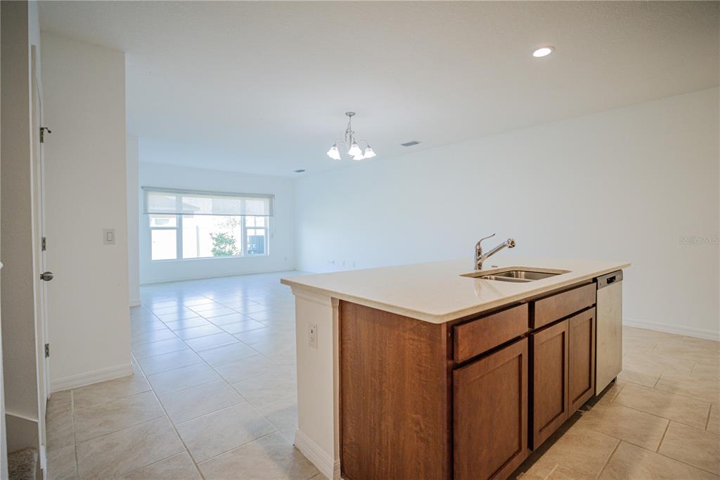 A kitchen island with a sink sits in the foreground of a bright, open-concept room — 1284 WISPY CYPRESS DRIVE, KISSIMMEE, FL