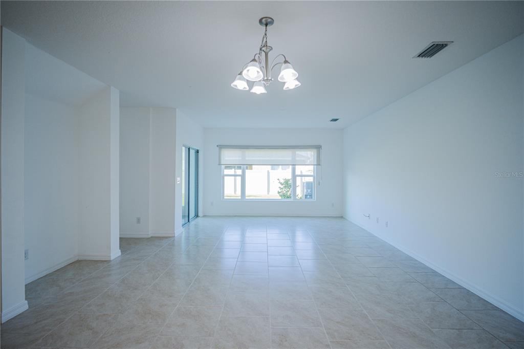 An empty room features white walls, light-colored tile flooring, a chandelier, and a large window — 1284 WISPY CYPRESS DRIVE, KISSIMMEE, FL
