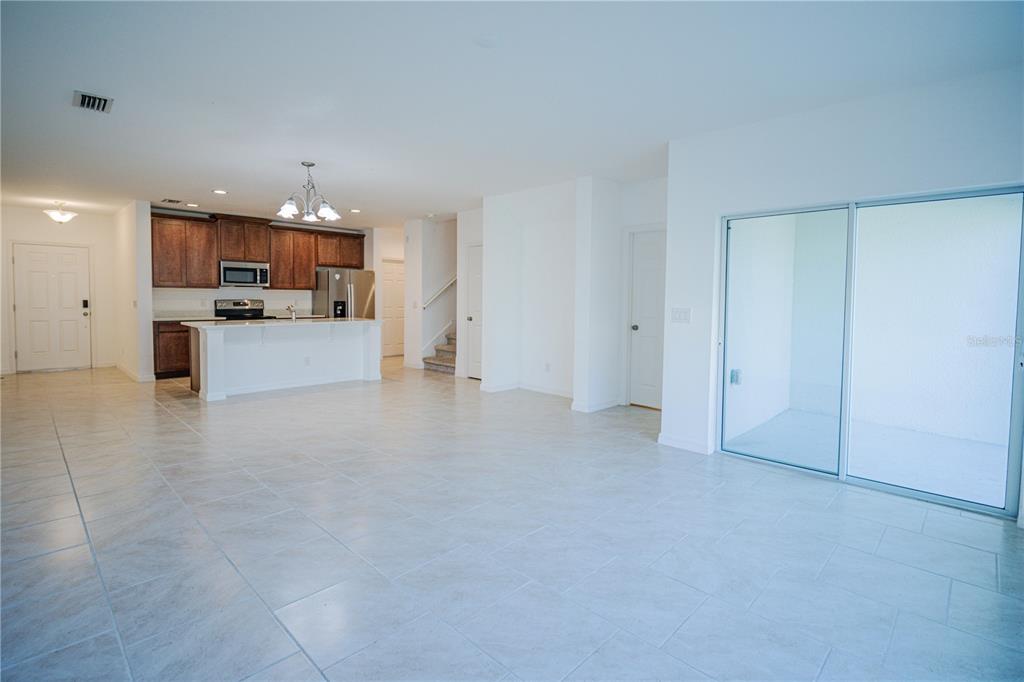 An open-concept kitchen and living area features tile flooring, dark wood cabinets, and sliding doors — 1284 WISPY CYPRESS DRIVE, KISSIMMEE, FL