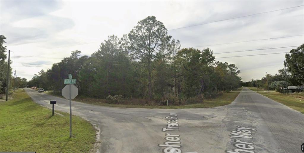 A vacant, wooded corner lot sits at the intersection of two paved residential streets — TBD FISHER WAY, OCKLAWAHA, FL