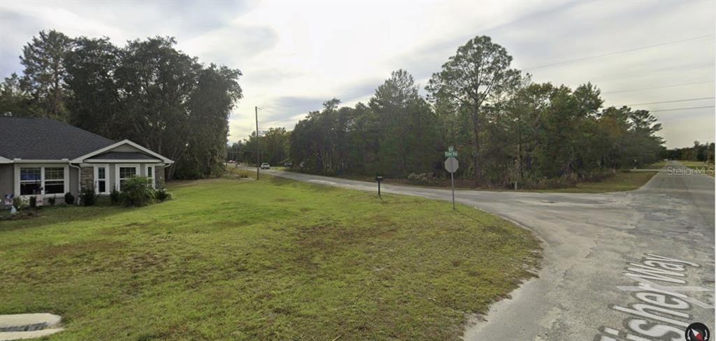 A grassy corner lot sits at the intersection of two paved roads near a house — TBD FISHER WAY, OCKLAWAHA, FL