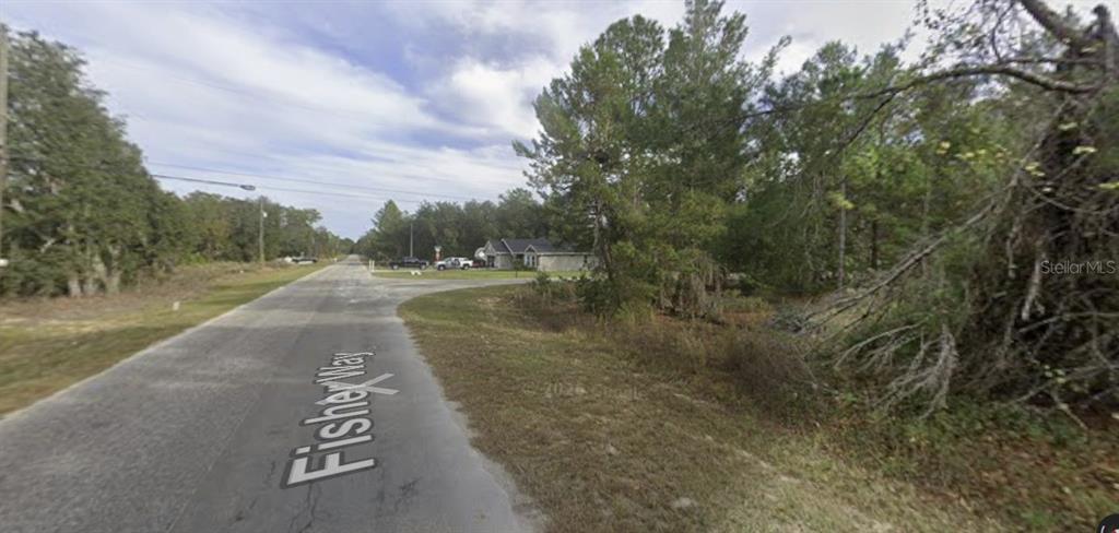 A paved road named Fisher Way leads toward a house surrounded by trees and brush — TBD FISHER WAY, OCKLAWAHA, FL