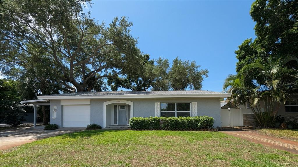A single-story gray house features a white garage door, a covered entryway, and mature trees — 6408 7TH AVENUE N, ST PETERSBURG, FL