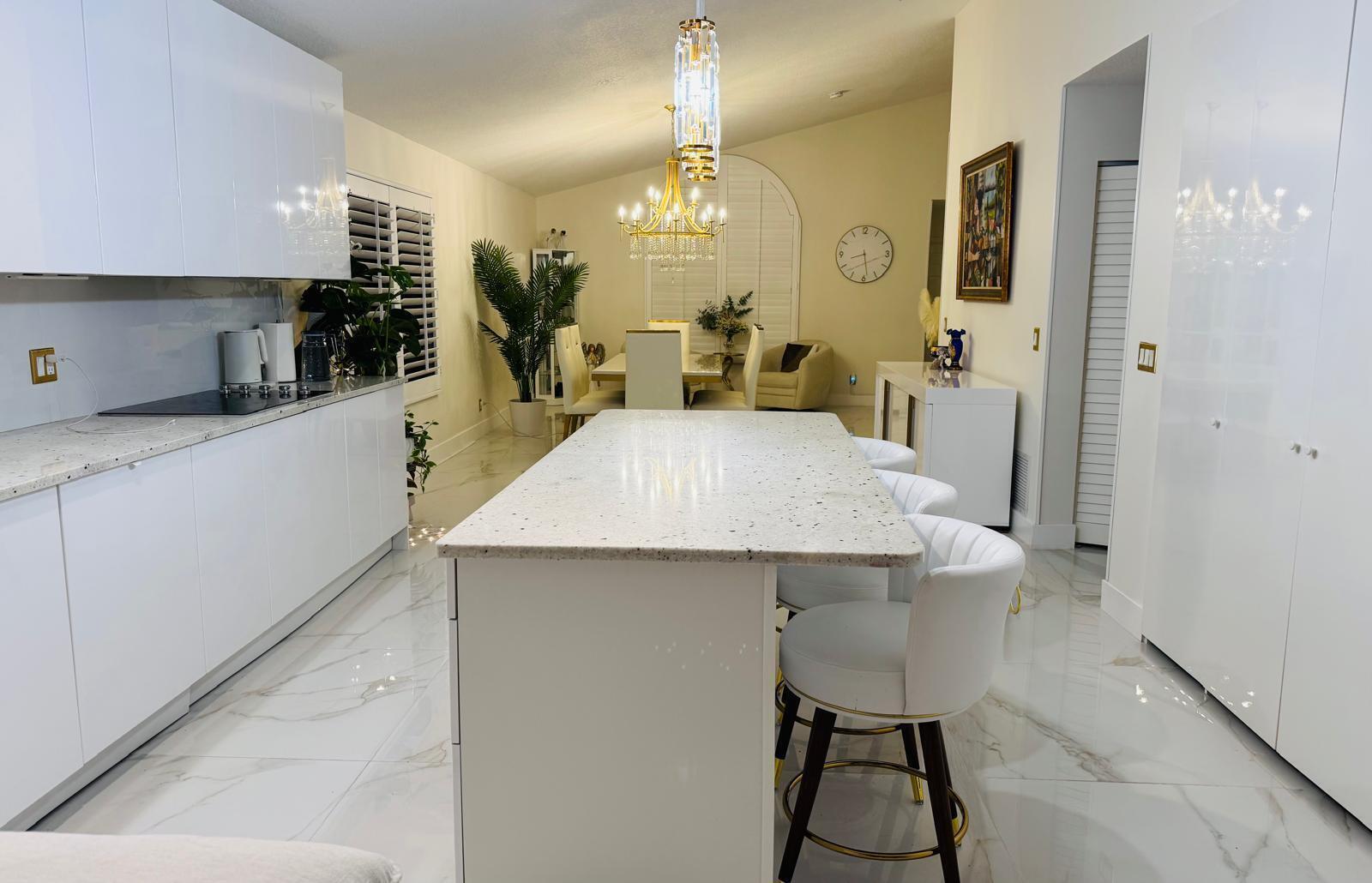 A modern white kitchen features a speckled stone island, bar stools, and marble-look tile flooring — 544 NW 38th Avenue, Deerfield Beach FL 33442, DEERFIELD BEACH, FL