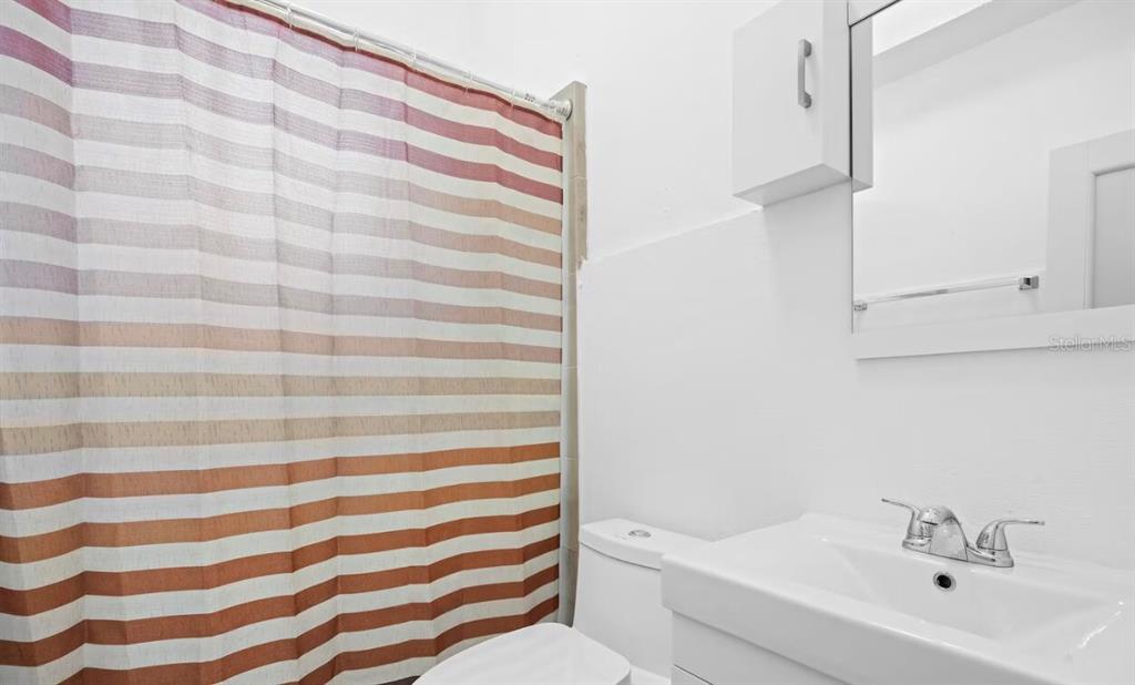 A bathroom features a striped shower curtain, a white toilet, and a vanity with a mirror — 250 CALLE DEL PARQUE UNIT 2A, SAN JUAN, PR