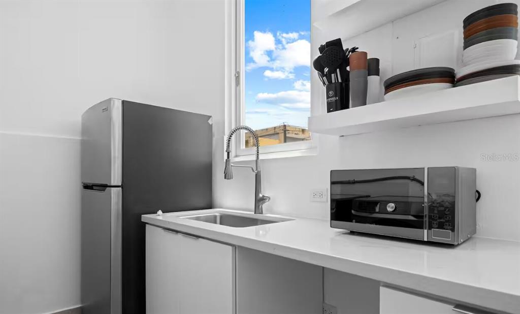 A small kitchen features a stainless steel refrigerator, sink, microwave, and white open shelving — 250 CALLE DEL PARQUE UNIT 2A, SAN JUAN, PR