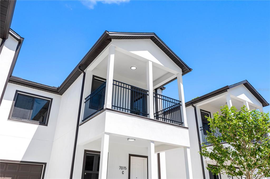 A low-angle exterior view shows a white two-story building with black trim and balconies — 7015 N CENTRAL AVENUE Unit C, TAMPA, FL