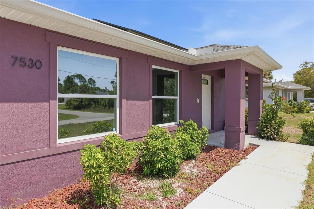 The exterior of a purple house features a concrete walkway and a small landscaped bed — 7530 FRANZINO AVENUE, NORTH PORT, FL