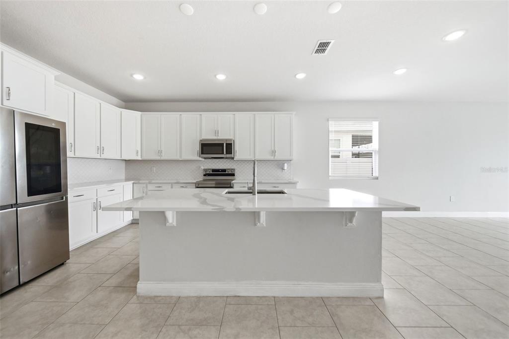 A modern kitchen features white cabinetry, stainless steel appliances, and a large marble-topped island — 1120 MATTIE POINTE BOULEVARD, AUBURNDALE, FL