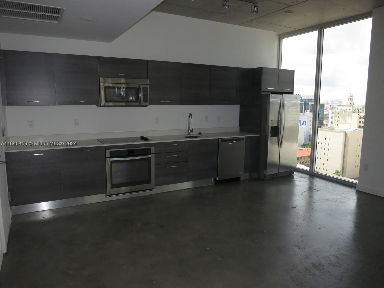 A modern kitchen features dark wood cabinetry, stainless steel appliances, and concrete floors with city views — 151 SE 1 St # 1902, Miami FL 33131, MIAMI, FL