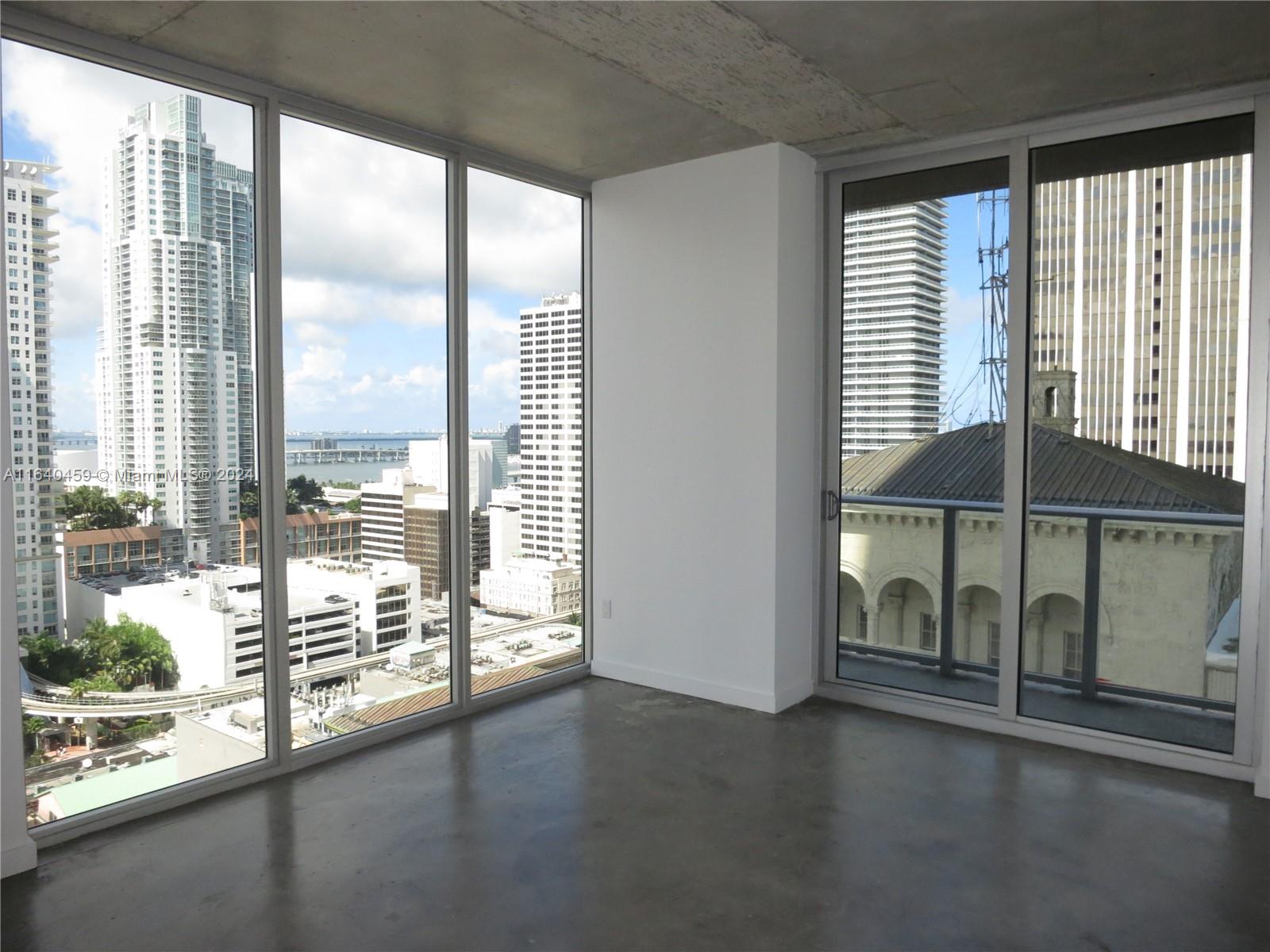 An unfurnished room with concrete floors, exposed ceiling, and floor-to-ceiling windows overlooking a city skyline — 151 SE 1 St # 1902, Miami FL 33131, MIAMI, FL