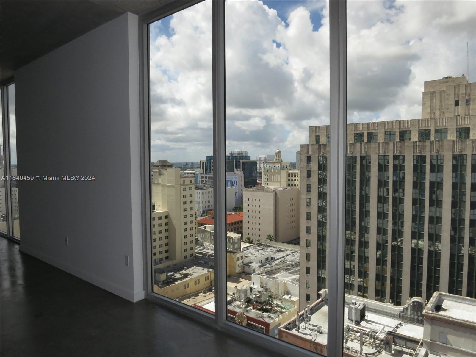 A room with floor-to-ceiling windows overlooking a dense urban cityscape with various high-rise buildings — 151 SE 1 St # 1902, Miami FL 33131, MIAMI, FL