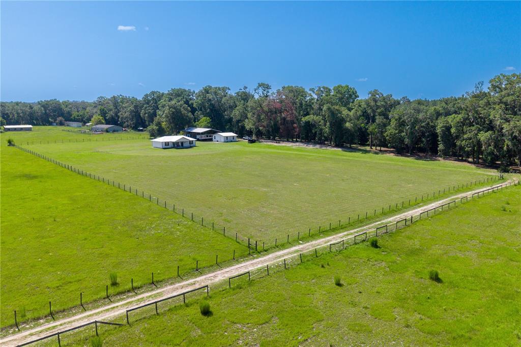 An aerial view shows a fenced pasture with a house and outbuildings near a forest — 21411 NW 209TH TERRACE, HIGH SPRINGS, FL