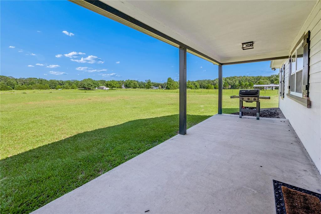 A covered concrete patio overlooks a large, open grassy field under a clear blue sky — 21411 NW 209TH TERRACE, HIGH SPRINGS, FL