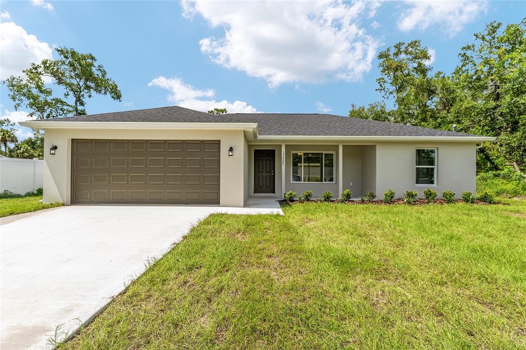 A single-story house with a tan exterior, a two-car garage, and a dark shingled roof — 13027 NE 5TH PLACE, SILVER SPRINGS, FL