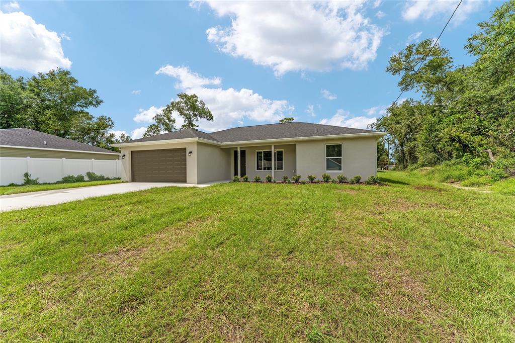 A single-story house with a beige exterior, a two-car garage, and a grassy front yard — 13027 NE 5TH PLACE, SILVER SPRINGS, FL