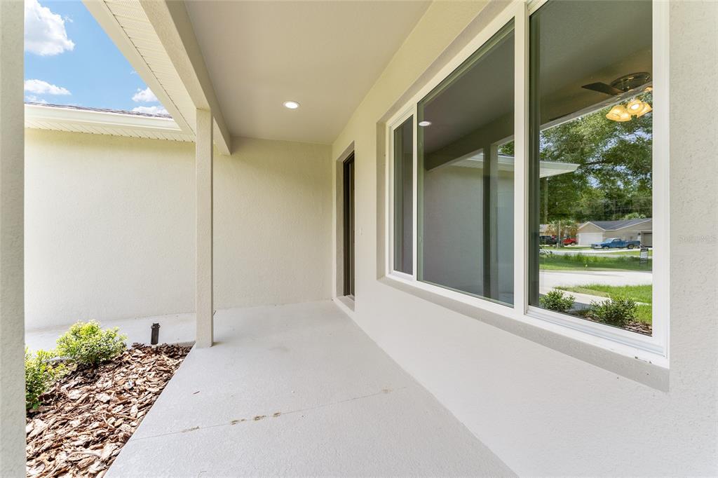 A covered concrete porch features a white ceiling, a recessed light, and large windows — 13027 NE 5TH PLACE, SILVER SPRINGS, FL