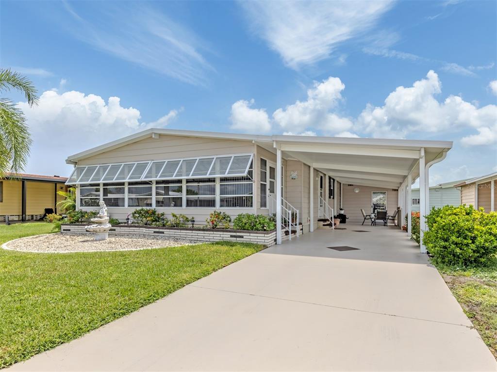 A single-story mobile home with a beige exterior, a carport, and a landscaped front yard — 182 PALM HARBOR DRIVE, NORTH PORT, FL