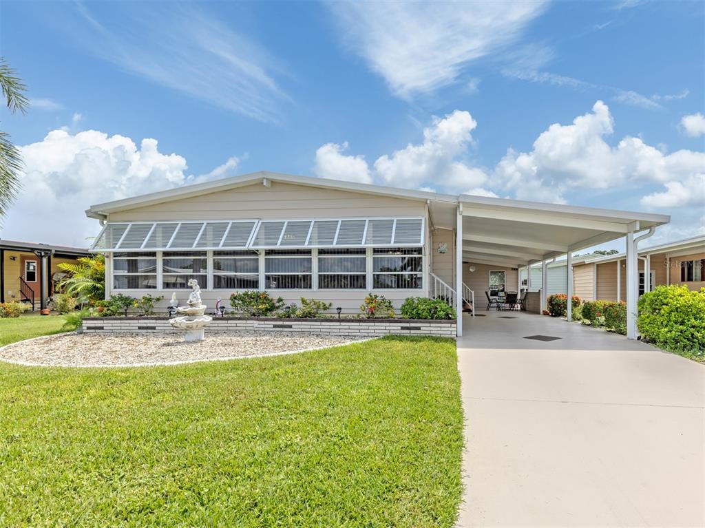 A single-story manufactured home with a carport, a front lawn, and a decorative fountain — 182 PALM HARBOR DRIVE, NORTH PORT, FL